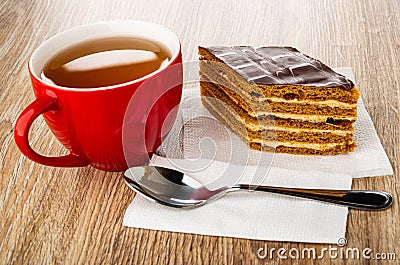 Cup of tea, piece of cake, spoon on paper napkin on wooden table Stock Photo