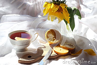 A Cup of tea with a slice of lemon, a sliced lemon on a Board, a bouquet of sunflowers on a white background in the sun with Stock Photo