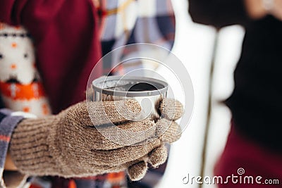 A cup of tea from a thermos on winter picnic in the woods. Woman hand`s in a warm gloves Stock Photo