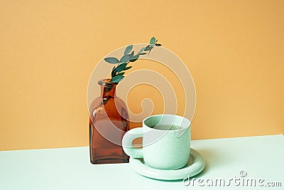 Cup of tea and vase of eucalyptus leaf on mint green table. orange background Stock Photo
