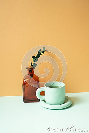 Cup of tea and vase of eucalyptus leaf on mint green table. orange background Stock Photo