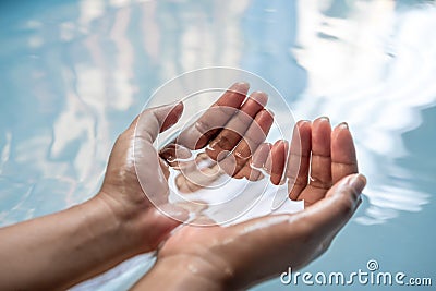 Cupped hands partially submerged in clear blue drinking water - Wet hands raised from a fresh water spring Stock Photo