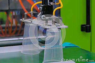 Cups on conveyor belt of plastic injection molding machine with robotic arm Stock Photo