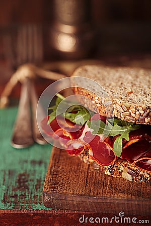 Cured meat sandwich with seeded bread on old wooden table Stock Photo