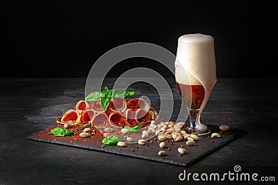 Cured prosciutto or balyk with pistachios, a spinach and a light beer with foam on a black background. Copy space. Pistachios and Stock Photo