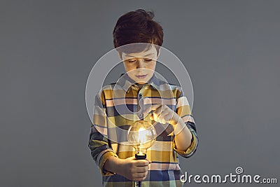 Boy touching glowing lightbulb lamp in hand stand on studio copy space Stock Photo