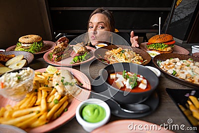 Curious anticipant woman blogger with lips in tube looking at abundance of snack tasty, delicious food for mukbang video Stock Photo