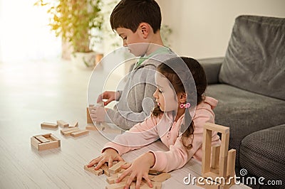 Curious beautiful Caucasian girl inspecting her brother`s wooden block buildings - childhood activities, fine motors skill Stock Photo