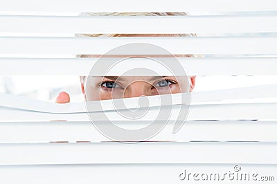 Curious blonde woman looking through venetian blind Stock Photo