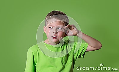 Curious boy listens. Closeup portrait child hearing something, parents talk, gossips, hand to ear gesture isolated on green. Stock Photo