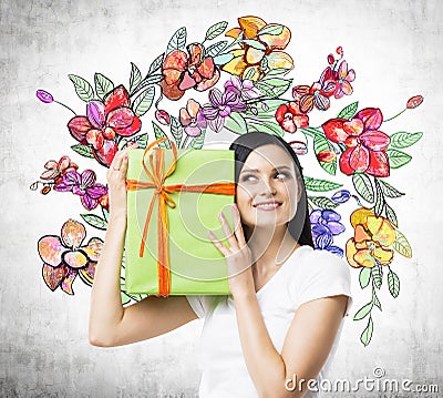 A curious brunette woman tries to guess what is inside the green gift box. Stock Photo