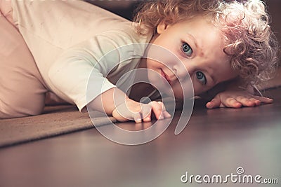 Curious cute child hiding under the bed in kids room and looking scared Stock Photo