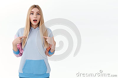 Curious excited blonde girl, teenage college student asking permition to participate, pointing fingers at herself, open Stock Photo
