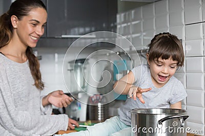 Curious girl playing with pot cooking with mom in kitchen Stock Photo