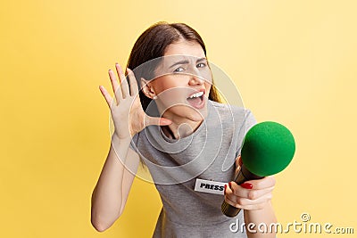 Emotional young girl, female press representative holding reporter microphone isolated on yellow studio background Stock Photo