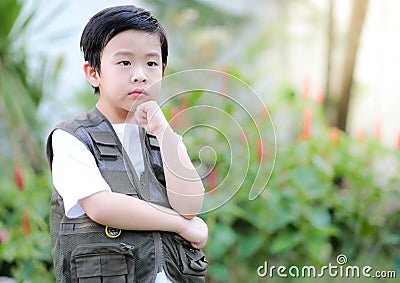 Curious little young Asian boy standing in the garden and touch his chin. Exploring the world, outdoors activity Stock Photo