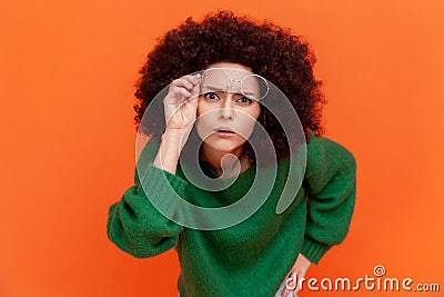 Curious woman with Afro hairstyle wearing green casual style sweater raising her optical glasses Stock Photo