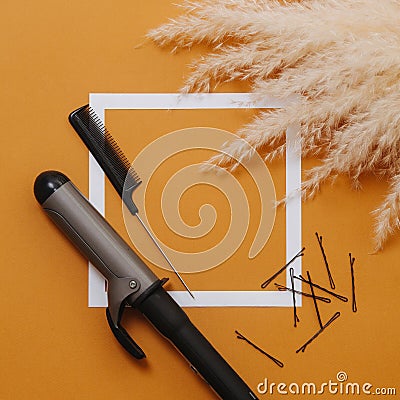Curling iron, rat tail comb and bobby pins over orange background. Top view Stock Photo