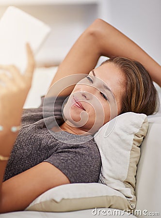 Curling up with a good e-book. a young woman relaxing on the sofa with a digital tablet at home. Stock Photo