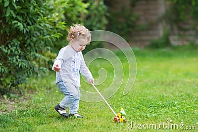 Curly baby girl playing in garden with wooden toy Stock Photo