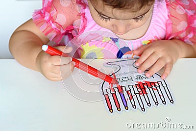 Curly brunette cute little toddler girl painting with color pen paper menorah and candle. Stock Photo