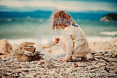 Curly child girl building stone tower on the beach Stock Photo