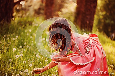 Curly child girl in pink fairytale princess dress gathering flowers in the forest Stock Photo