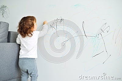 Curly cute little baby girl drawing with crayon color on the wall. Works of child Stock Photo