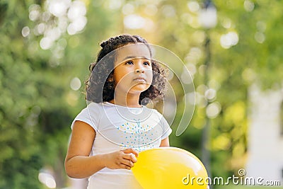 Curly cute sad hispanic dark skinned girl kid play with yellow balloon outdoor in summer. Summer, childhood, leisure Stock Photo