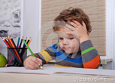 Curly European boy draws sitting at table Stock Photo