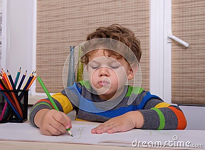 Curly European boy draws sitting at table Stock Photo