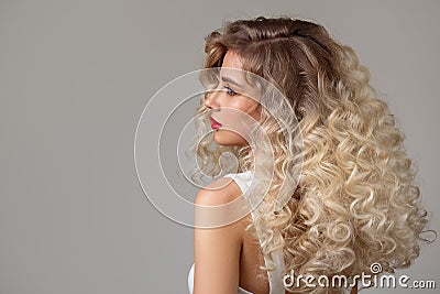 Curly fashion blonde woman with long hair and makeup. Back view. Grey background Stock Photo