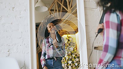 Curly funny african american girl dancing and singing with hair dryer in front of mirror at home Stock Photo