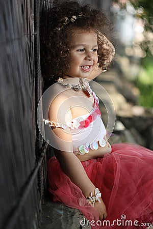 Curly girl in a pink dress with shell decorations on the nature Stock Photo