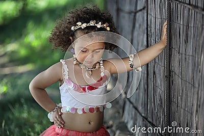 Curly girl in a pink dress with shell decorations on the nature Stock Photo