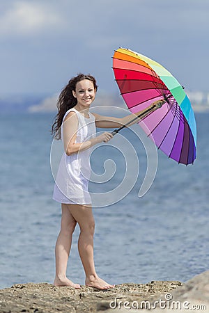 Curly girl in white sleeveless dress closes rainbow umbrella Stock Photo