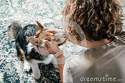 Curly cheerful woman with dog corgi sitting, relaxing and playing on floor at home. Weekend leisure activities Stock Photo