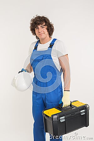 Curly haired builder lifting up toolbox and white helmet in studio. Stock Photo