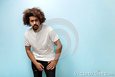 A curly-headed brunet man is leaning forwards wearing white T-shirt and ripped jeans. The guy is holding hands on the Stock Photo