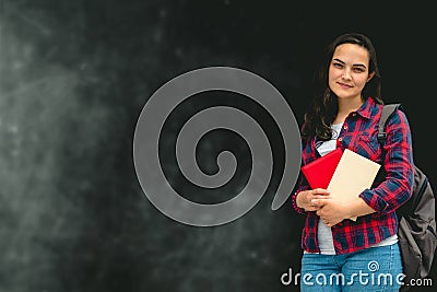 Woman wearing casual shirt and jeans and backpack holding books on a background of chalkboard with place for text Stock Photo