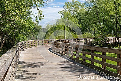 Curve ahead on an empty elevated boardwalk running through forest and wetlands, public use walking trail Stock Photo