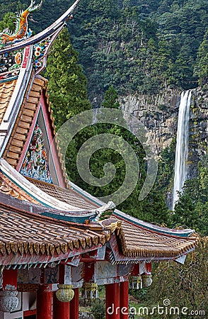 Curved roofs of colorful Chinese temple and Nachi waterfalls on the background. Wakayama. Japan Stock Photo