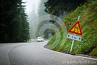 Curvy mountain road with slippery route sign and blurred white car in the background Stock Photo