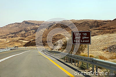 Curvy sandy road on a highway that runs along the Dead Sea from one side and Edom Mountains at Arava Desert from the other in Stock Photo