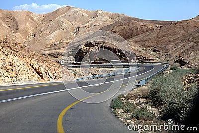 Curvy sandy road on a highway that runs along the Dead Sea from one side and Edom Mountains at Arava Desert from the other in Stock Photo