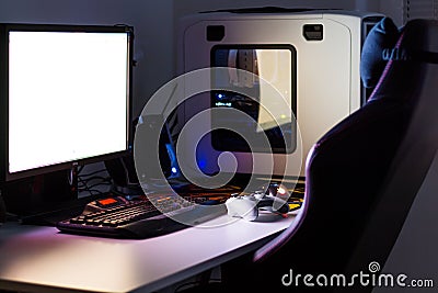 Custom built desktop computer for gaming on the table with joystick, monitor, keyboard, chair under low light. Selective focus. Stock Photo