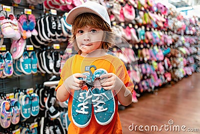 Customer child holdind shoes, shopping at supermarket, kids shoes store. Stock Photo