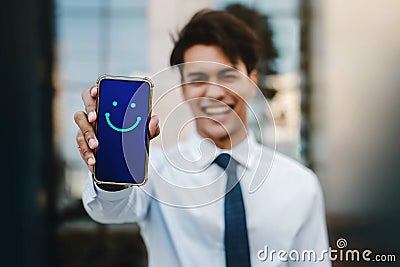 Customer Experiences Concept. Young Businessman Giving a Happy Face Icon and Positive Review via Smartphone. Client`s Satisfactio Stock Photo