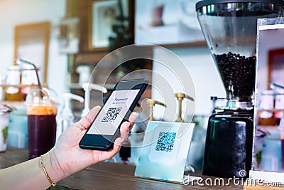 Customer hand using smart phone to scan Qr code payment tag with blurry coffee grinder in coffee shop to accepted generate Stock Photo