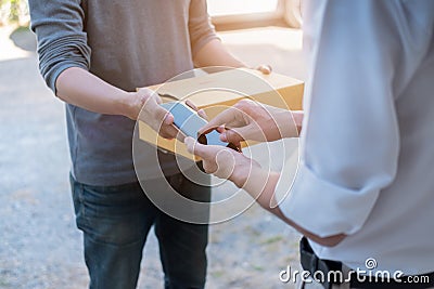 Customer hands appending signature in mobile phone, man receiving parcel post box from courier with delivery service man, express Stock Photo